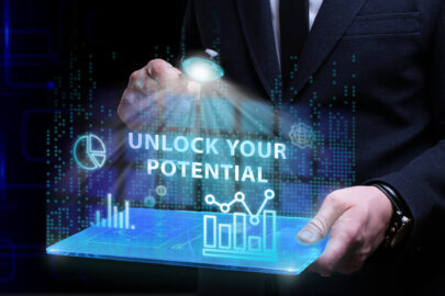 Homem de camisa social clara, gravata escura e blazer escuro. Na mão esquerda, ele segura um tablet. Na mão direita, ele segura um lupa. Entre a lupa e o tablet, há uma tela virtual com a expressão “Unlock Your Potential”.